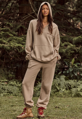 a-woman-stands-outdoors-in-a-wooded-setting-wearing-a-matching-beige-hooded-sweatshirt-and-jogger-pants-set-with-red-lace-up-ankle-boots