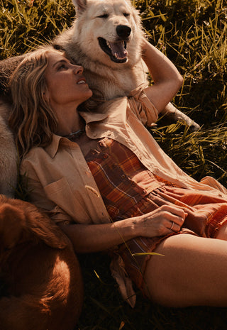 A woman lying in grass outdoors with a large white dog behind her and a brown dog at her side