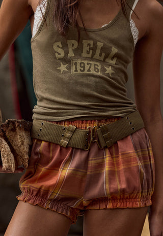 a-close-up-of-a-person-wearing-an-olive-green-ribbed-tank-top-with-spell-1976-printed-on-the-front-paired-with-rust-orange-plaid-bloomers-and-a-wide-olive-belt