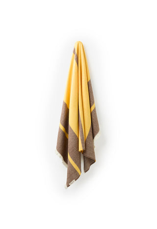 a-folded-striped-scarf-in-yellow-and-brown-hangs-against-a-plain-white-background